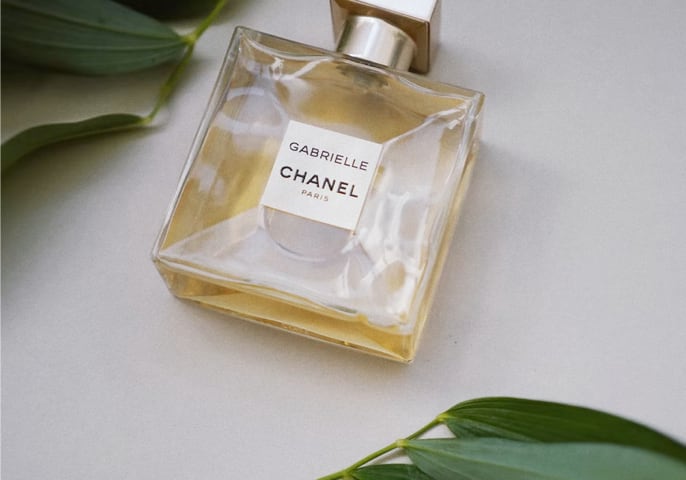 Square shaped glass perfume bottle with a gold cap, filled with amber-colored liquid and labeled 'Gabrielle Chanel'